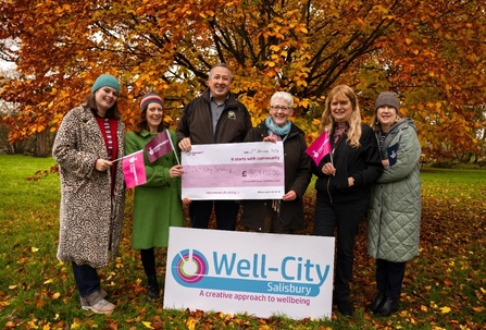 A group of people standing underneath a tree holding a cheque